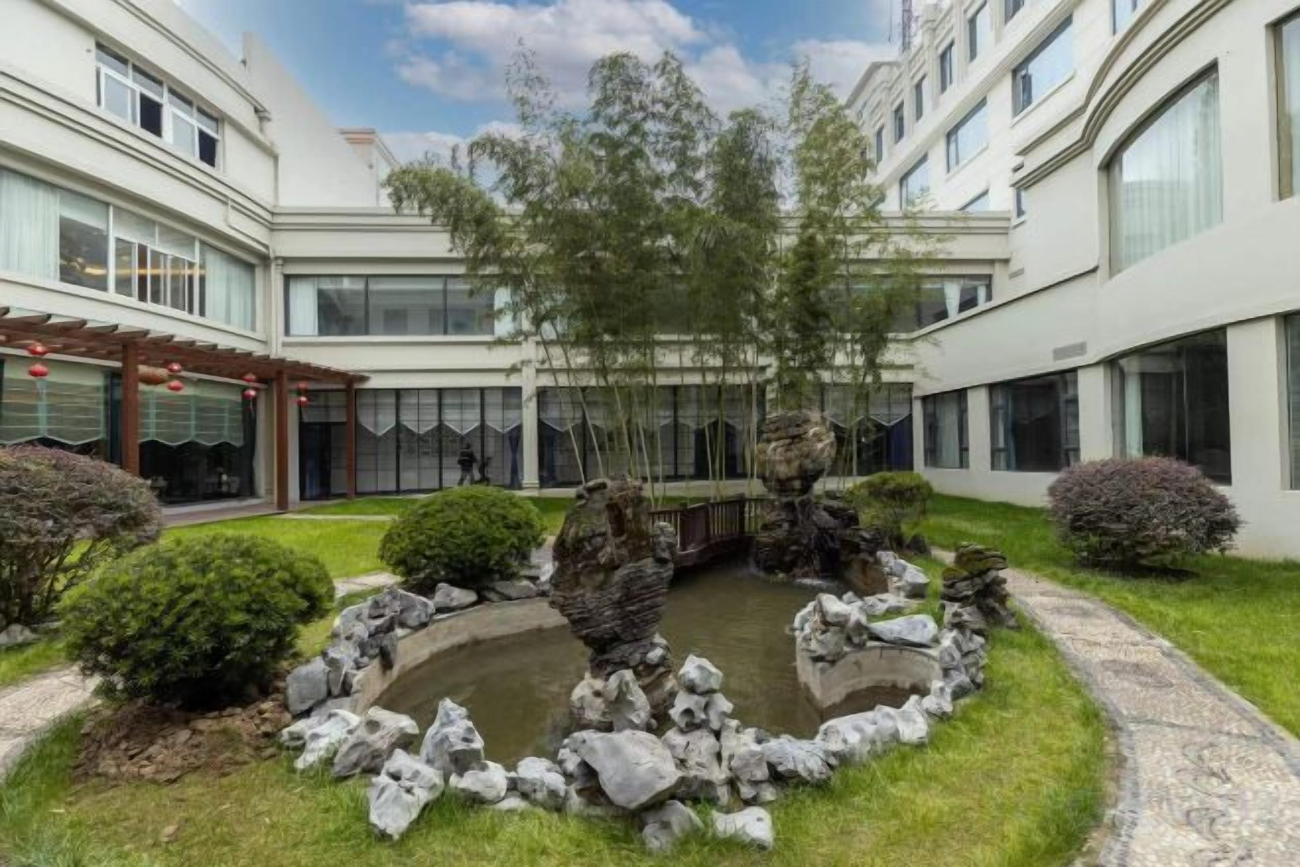 A courtyard with a pond, rock formations, and a pergola.