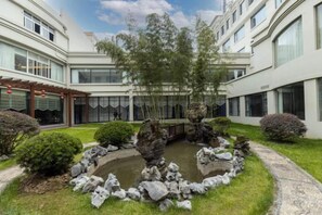 A courtyard with a pond, rock formations, and a pergola. - Xiang Yuan Hotel (Cixi)