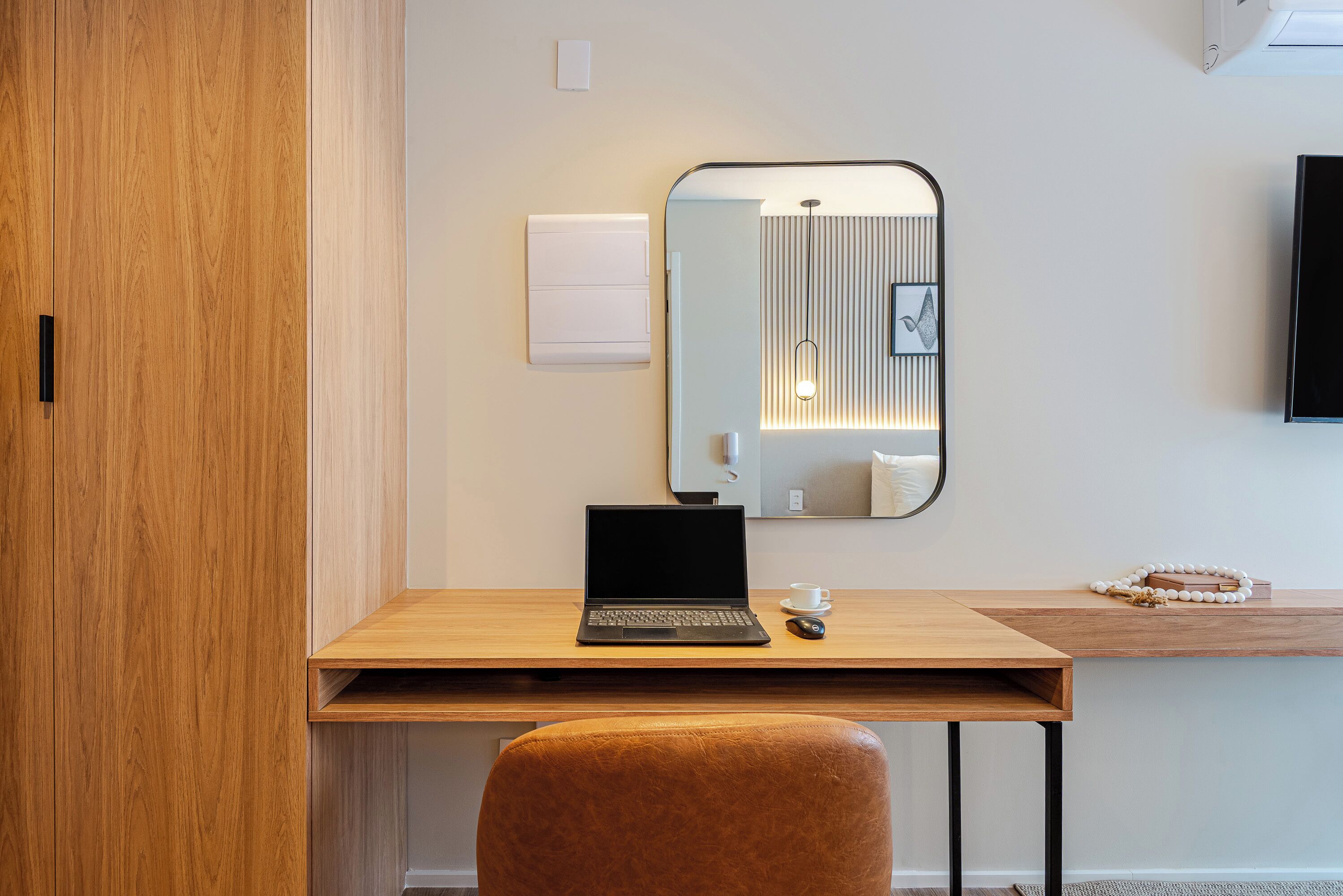 Una habitación de hotel moderna con un escritorio de madera, una computadora portátil, una taza y un espejo.