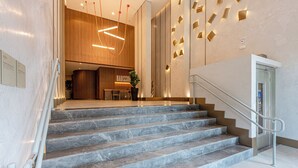 A modern hotel lobby with marble stairs, a reception desk, and a staircase with a handrail.