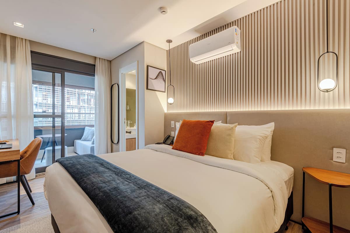 Ett modernt hotellrum med en stor säng, ett skrivbord och utsikt över staden genom fönstret.