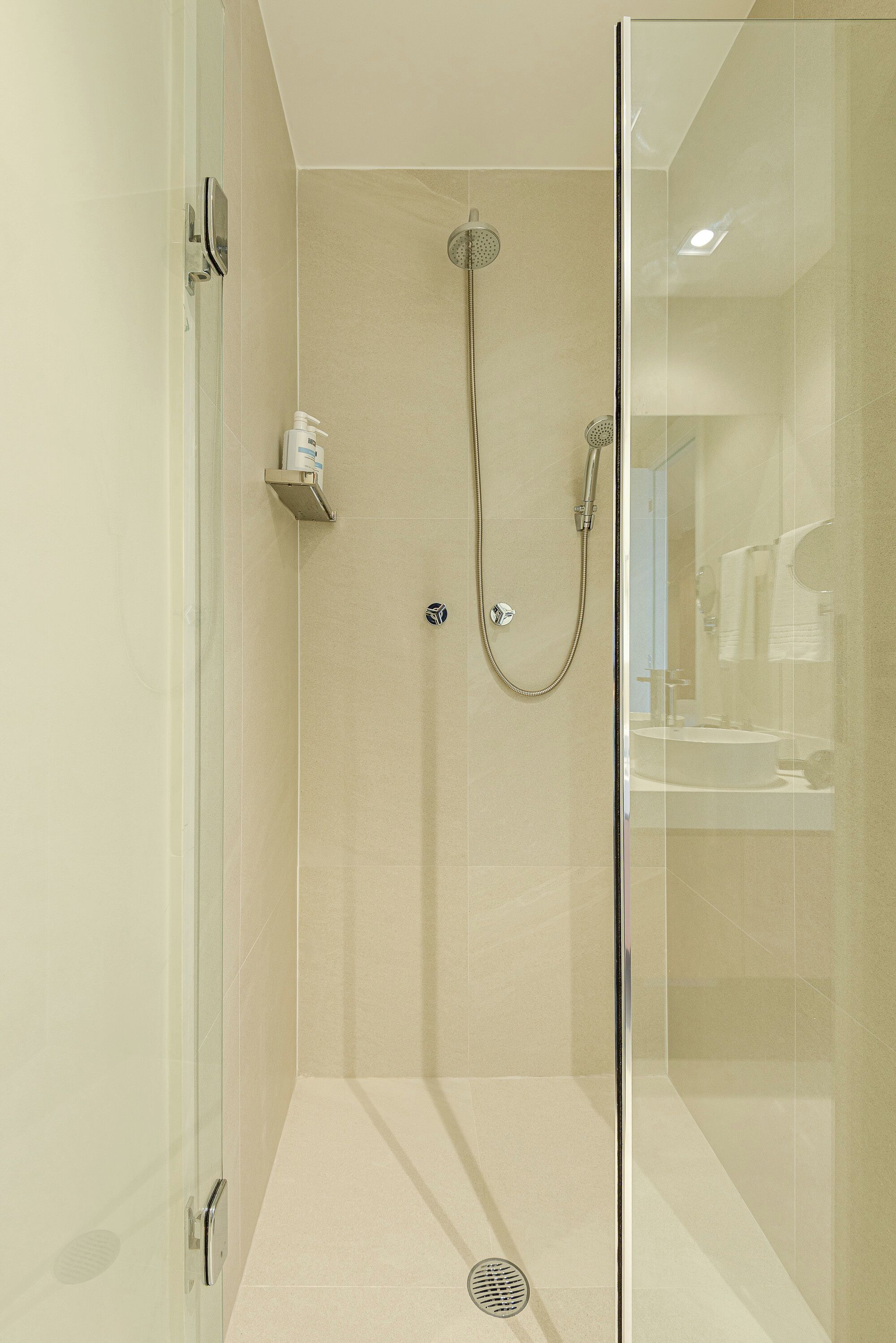 A modern bathroom with a glass shower enclosure, a handheld showerhead, and a wall-mounted faucet.