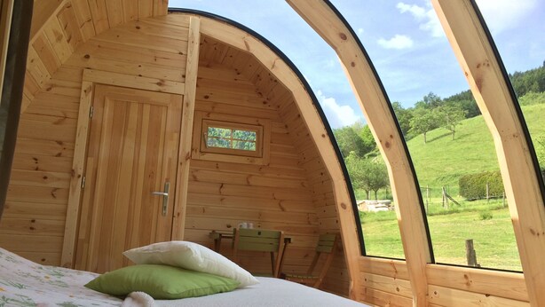 Una habitación acogedora de madera con una cama, una mesita y un ventanal con vistas a un paisaje verde.