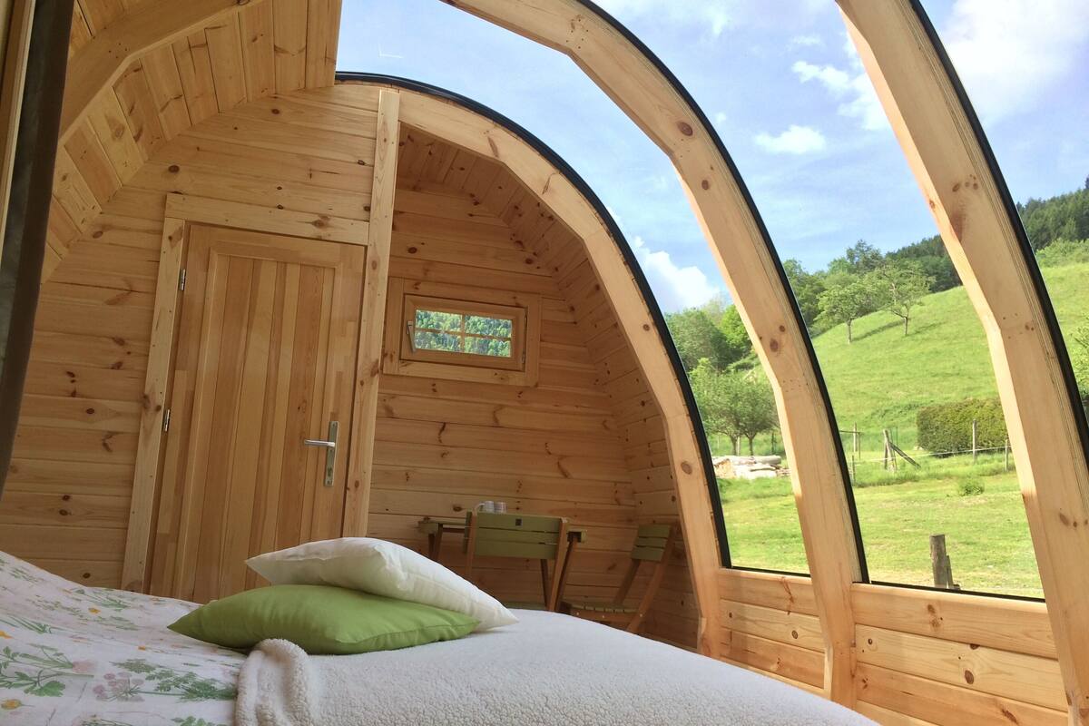 Una habitación acogedora de madera con una cama, una mesita y un ventanal con vistas a un paisaje verde.