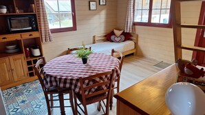 Una habitación acogedora con una cama de madera, una mesa de comedor con sillas, una pequeña cocina con microondas y una ventana con cortinas.