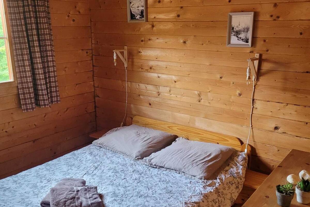 Una habitación cálida de cabaña de madera con una cama, un escritorio pequeño y una ventana con cortinas.