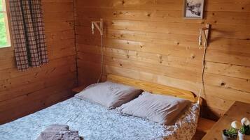 Een knus houten kamer met een bed, een klein bureau en een raam met gordijnen.
