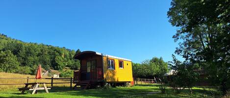 A yellow train car converted into a cabin with a small porch, surrounded by a grassy area and trees.