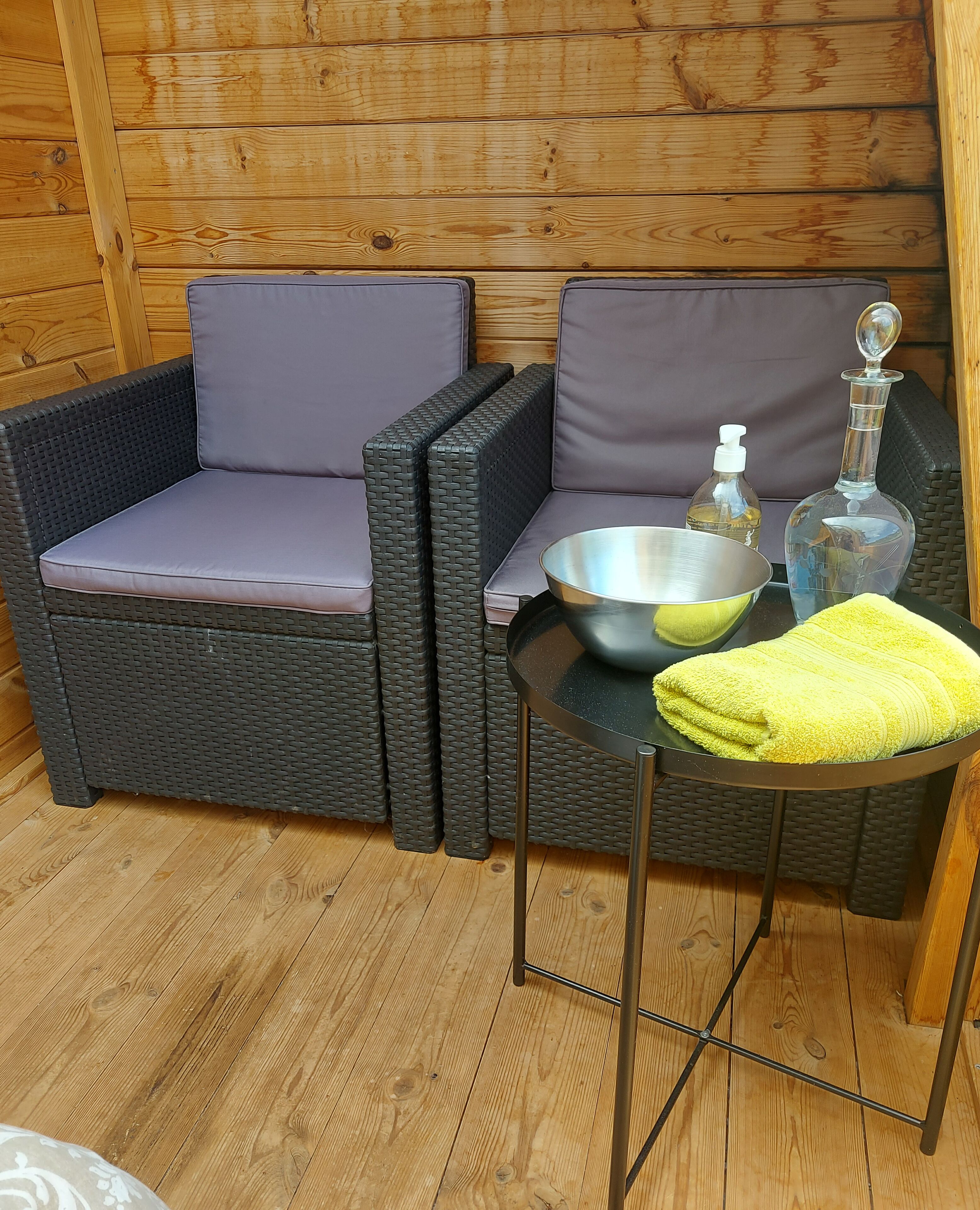 A wicker sofa with cushions, a metal bowl, a bottle of hand sanitizer, and a yellow towel on a small table.
