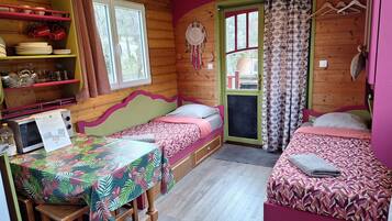 A cozy cabin-style room with two beds, a wooden table, and a shelf with dishes and mugs.