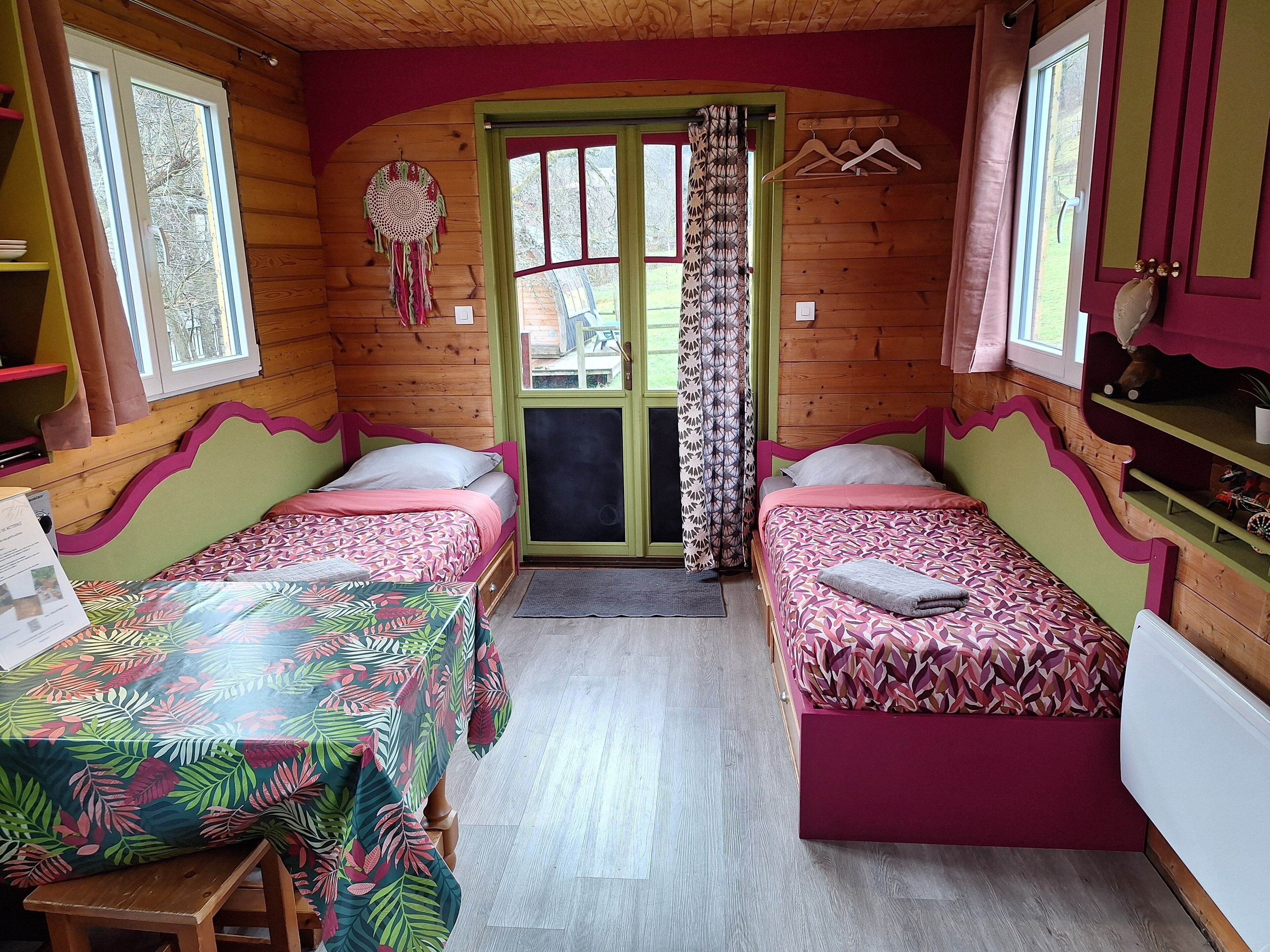 A cozy cabin room with two beds, a wooden ceiling, and a green door.