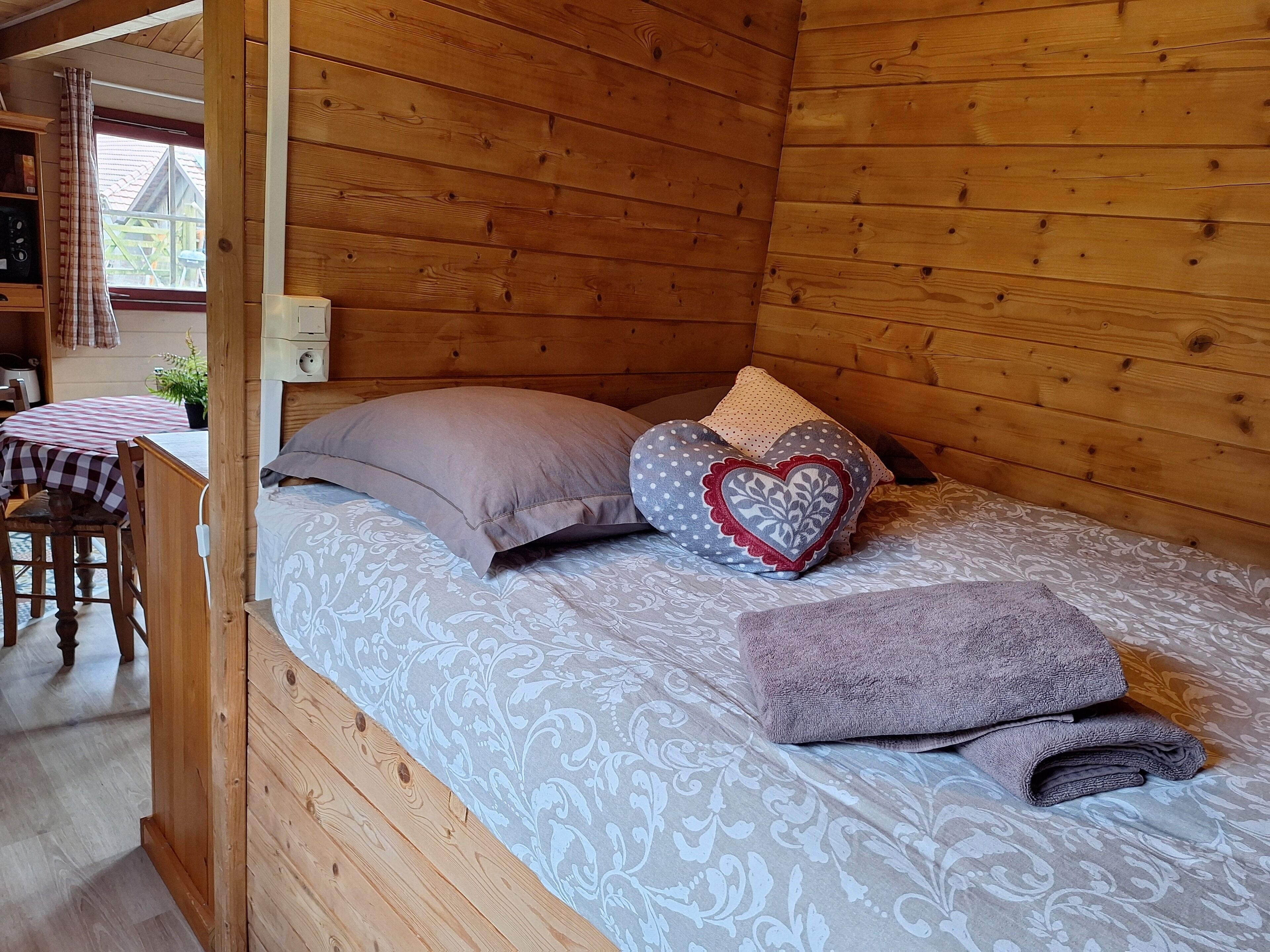 A cozy wooden cabin room with a bed, pillows, and a small table with a checkered tablecloth.