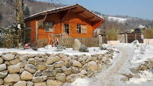 Una cabaña de madera con un muro de piedra al frente, rodeada de nieve y árboles.