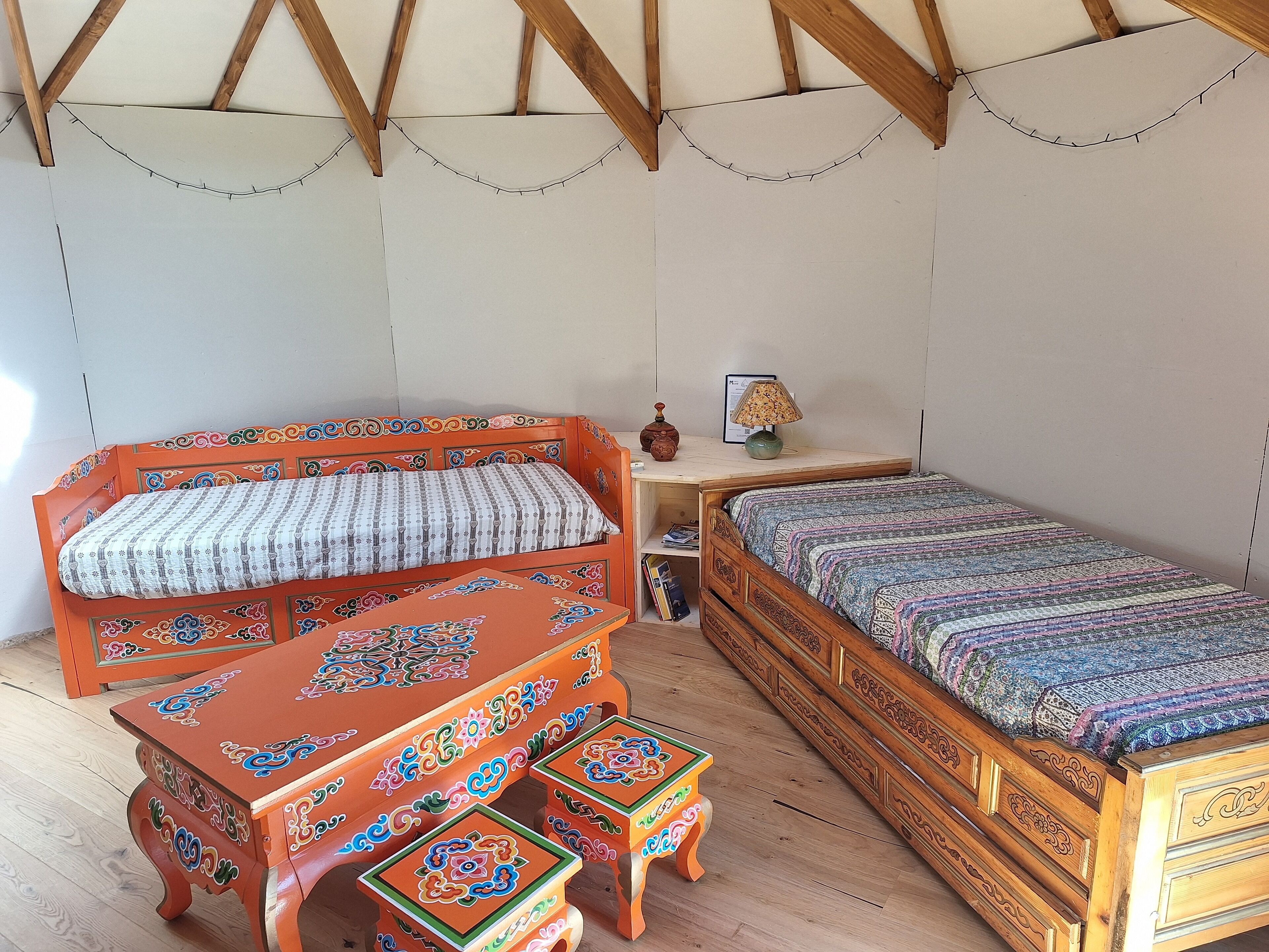 A room with a wooden bed, a wooden bench, and a small table with a lamp.