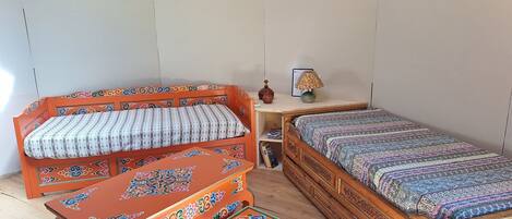 A room with a wooden bed, a wooden bench, and a small table with a lamp.