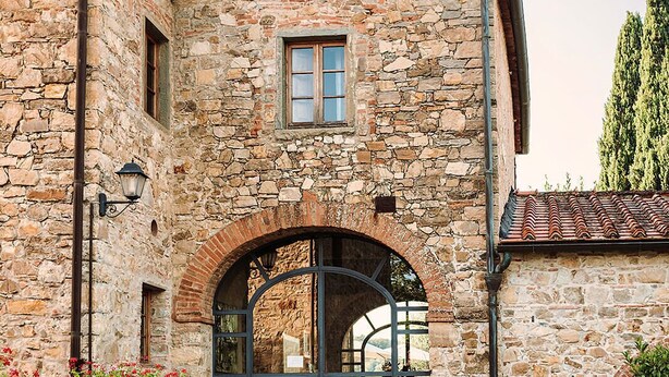 A stone building with an arched entrance, potted plants, and a tiled roof.