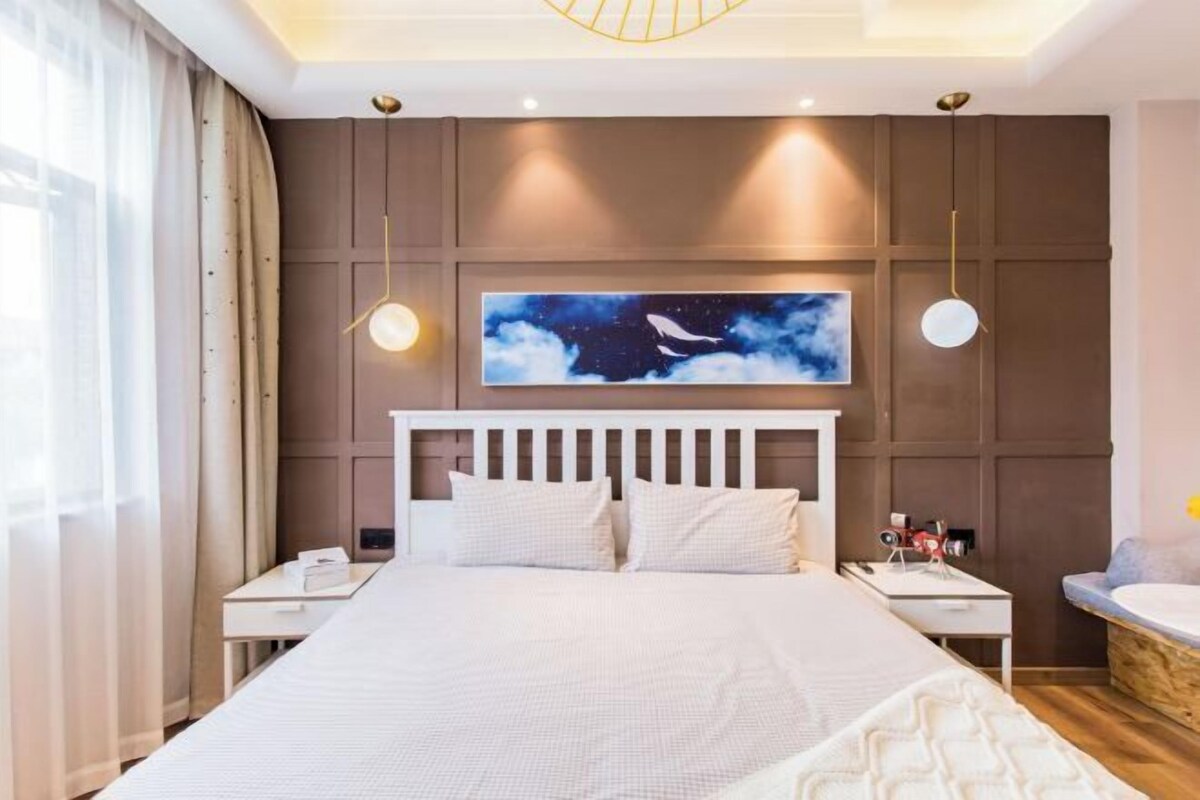 Quarto moderno com uma cama grande, mesa de cabeceira, luminária de teto e televisão fixada na parede.
