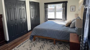 A bedroom with a bed, a window with curtains, a bedside table, and a door. - Cozy Cottage House in Louisville (Louisville)