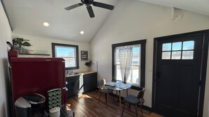 A compact kitchen with a ceiling fan, a refrigerator, a coffee maker, and a microwave. There is a dining area with a table and chairs, and a window with a view of the outside. - Cozy Cottage House in Louisville (Louisville)