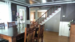 Un espace repas avec une table et des chaises en bois, un escalier et une porte donnant sur une autre pièce.