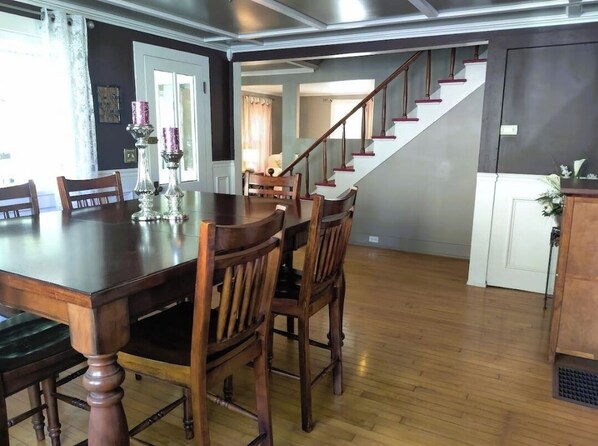 A dining area with a wooden table and chairs, a staircase, and a door leading to another room.