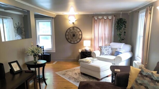 Un salon avec un canapé blanc, un divan marron, une petite table avec une lampe et une horloge murale décorative.
