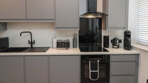 A modern kitchen with grey cabinets, a black range hood, a Bosch dishwasher, and a coffee maker. - 2 Bedroom Deluxe (Scarborough)