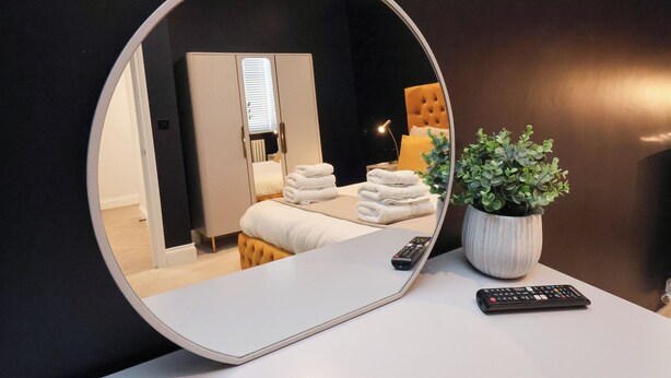 A round mirror reflecting a bedroom with a bed, a bedside table, a potted plant, and a remote control. - 2 Bedroom Deluxe (Scarborough)
