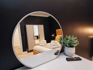 A round mirror reflecting a bedroom with a bed, a bedside table, a potted plant, and a remote control. - 2 Bedroom Deluxe (Scarborough)