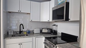 Una cocina compacta con gabinetes blancos, microondas, tostadora, licuadora y estufa.