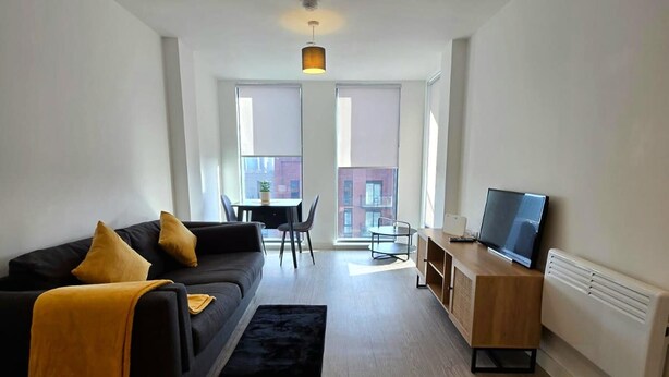 A modern living room with a black sofa, a small black rug, a wooden desk with a TV, and a dining area with a table and chairs.