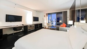 A modern hotel room with a large bed, a desk, two TVs, a chair, a sofa, and a view of the city. - Palms Place Hotel StripView (Las Vegas)