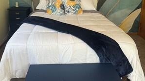 A bed with a large leaf-patterned headboard, a bedside table, and a bench in front of the bed.