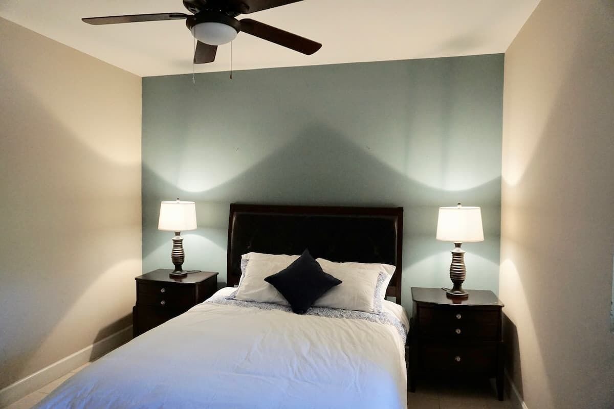 Une chambre à coucher avec un lit, deux tables de chevet avec des lampes, un ventilateur de plafond et un mur de couleur claire.