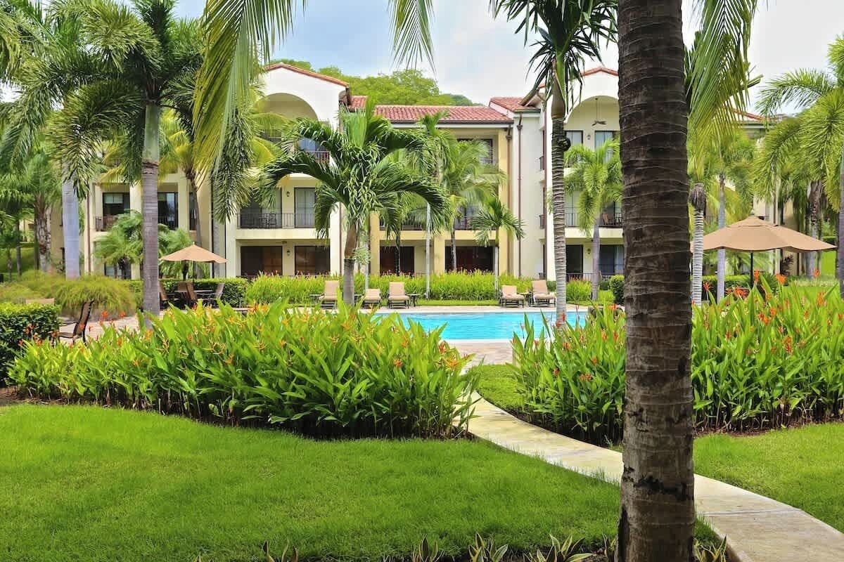 A resort with a swimming pool, palm trees, and a well-maintained garden.