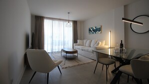 A modern living room with a glass dining table, white sofas, and a large window with curtains. - Happy Travel Daphne Higueron (Fuengirola)