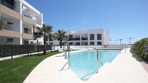 A modern apartment building with a swimming pool, palm trees, and a clear blue sky. - Happy Travel Daphne Higueron (Fuengirola)