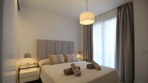 A modern hotel room with a large bed, a bedside table with a lamp, and a hanging light fixture. - Happy Travel Daphne Higueron (Fuengirola)