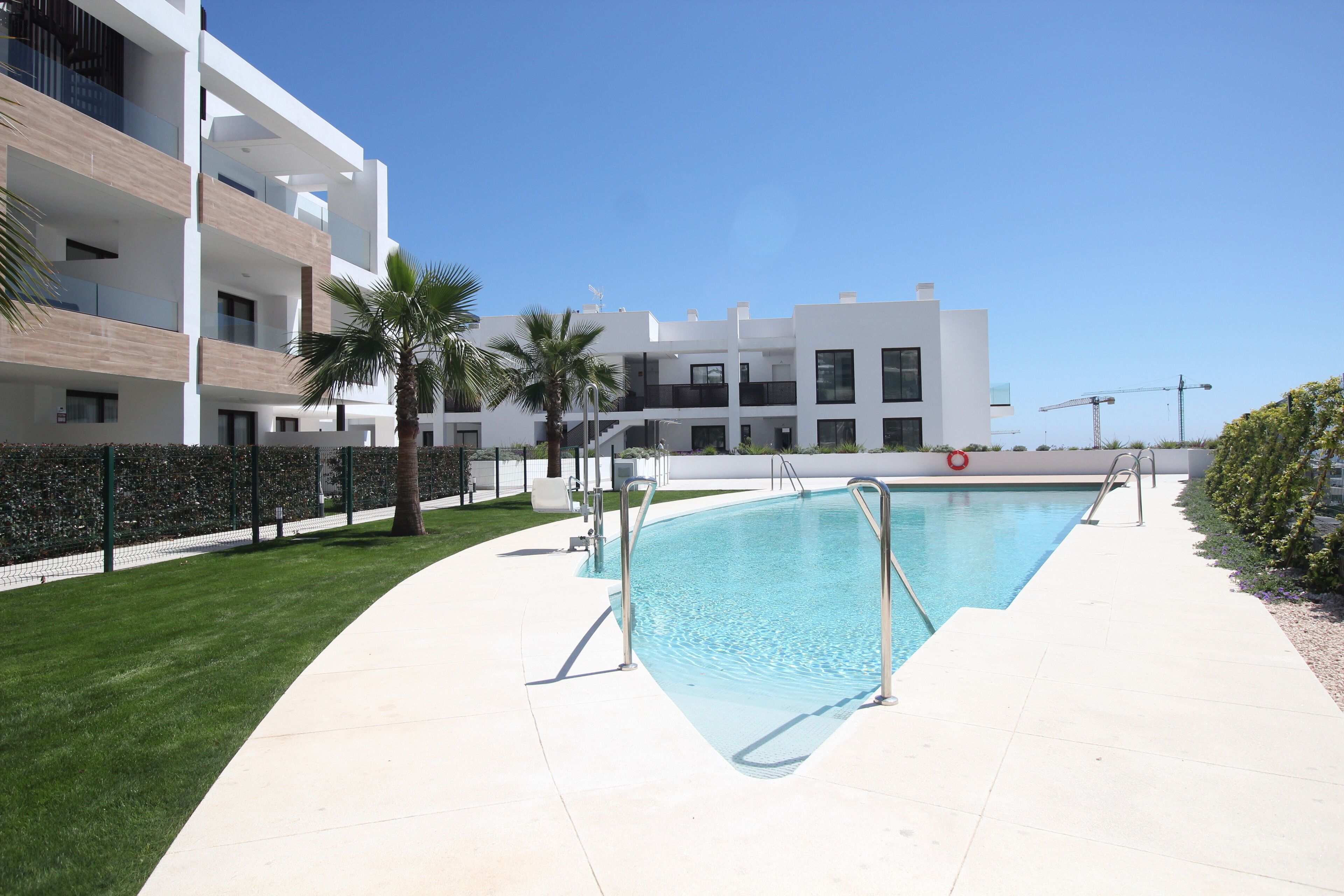 Un moderno condominio con piscina, palme e cielo azzurro intenso.