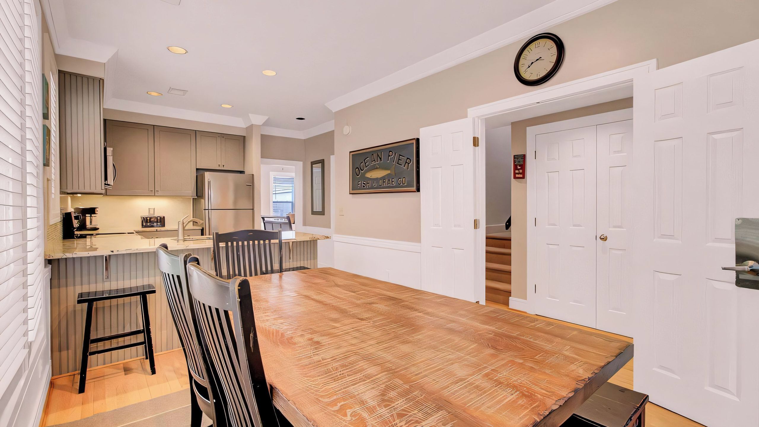 A modern kitchen with a wooden dining table, built-in cabinets, and a clock on the wall.