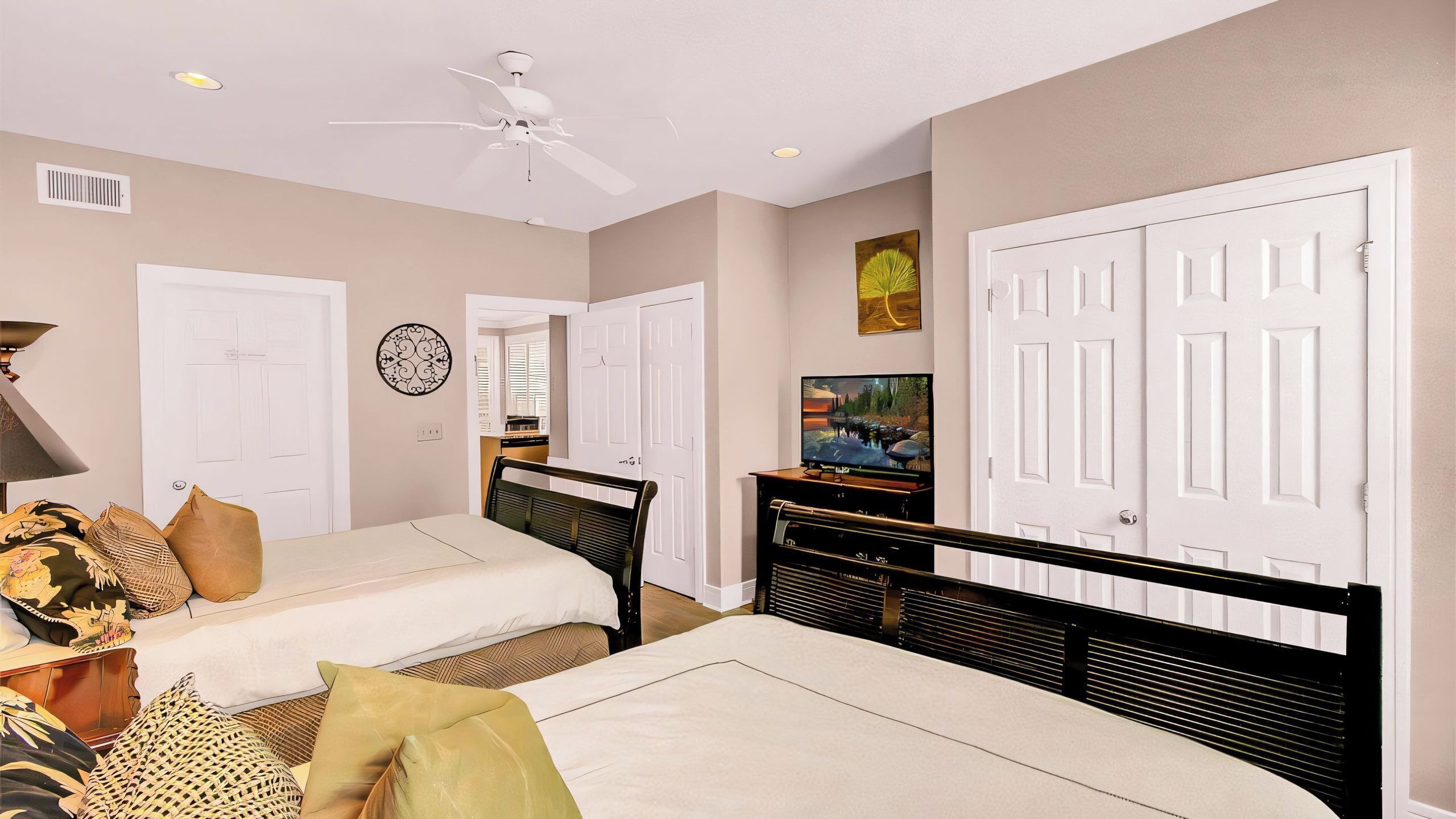 A bedroom with two beds, a TV, a ceiling fan, and a view of the kitchen.