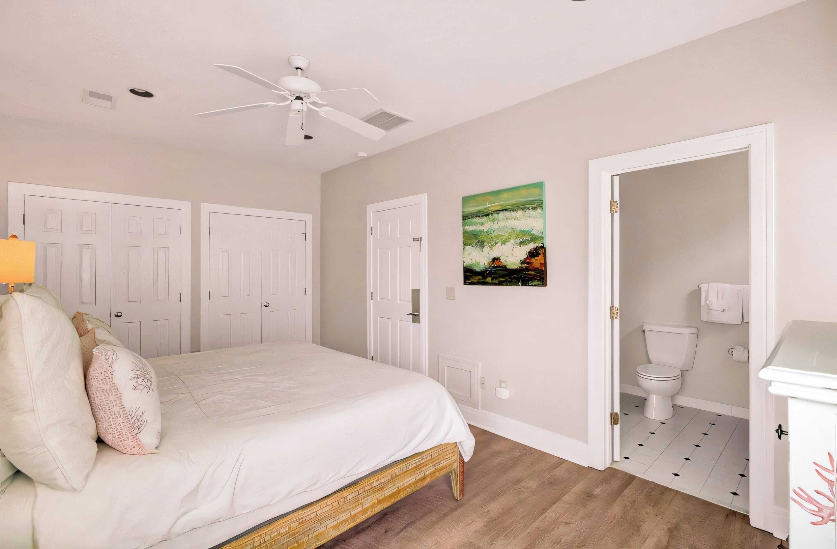 A bedroom with a bed, a ceiling fan, and a door leading to a bathroom.