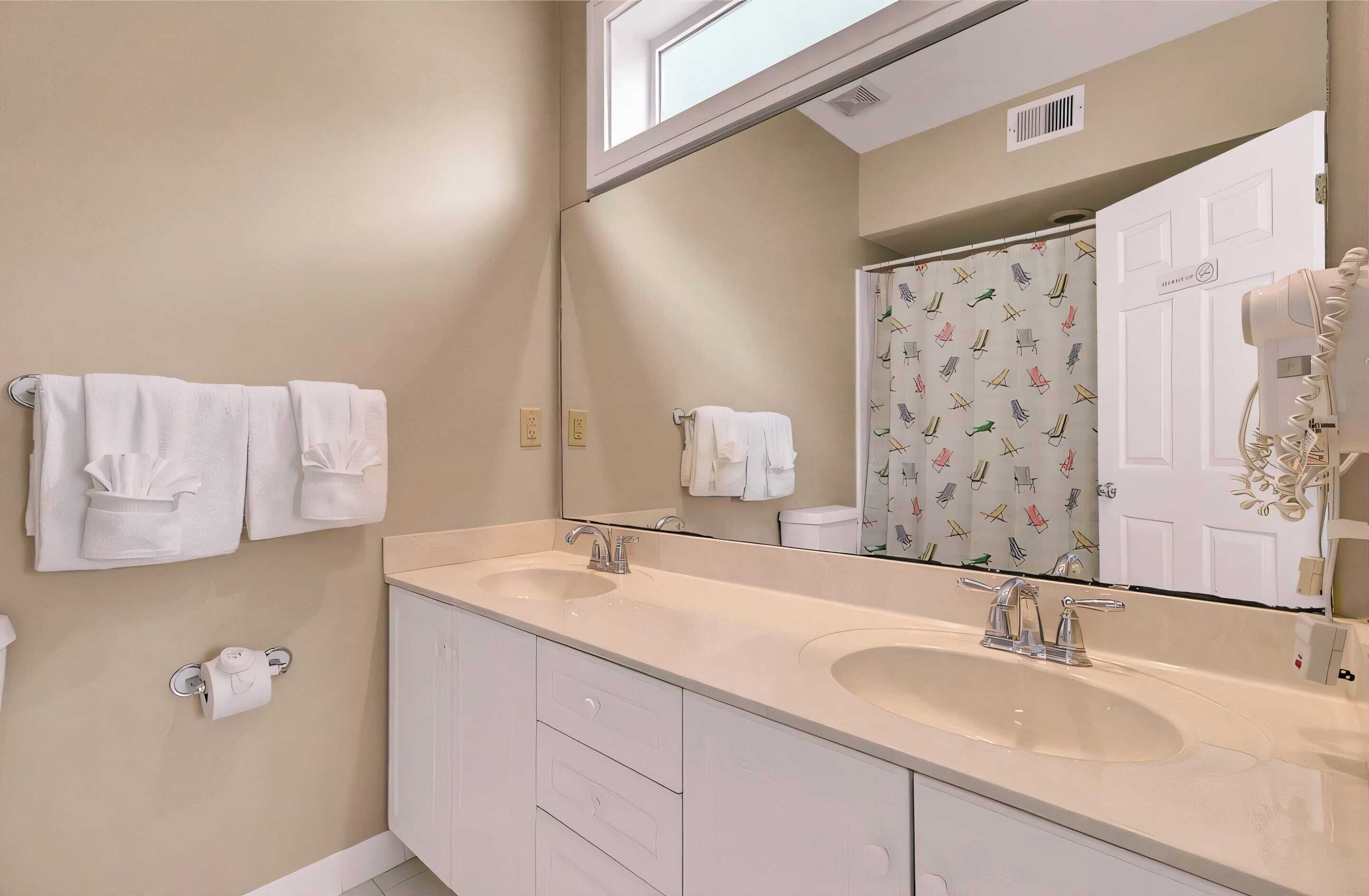 Baño con dos lavamanos, un espejo grande y una ducha con cortina estampada.