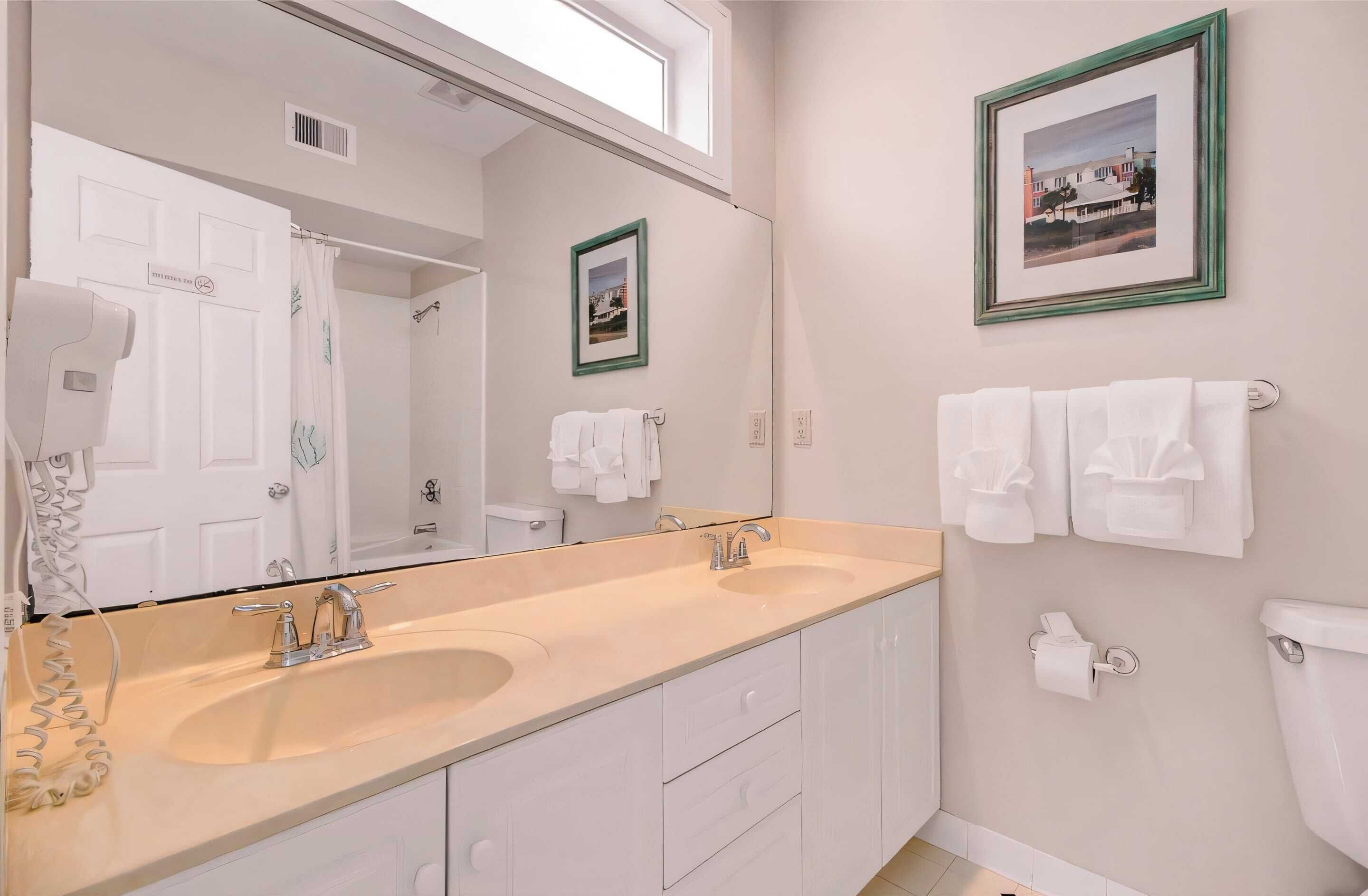 Un baño con lavamanos doble, un espejo grande y dos cuadros enmarcados en la pared.