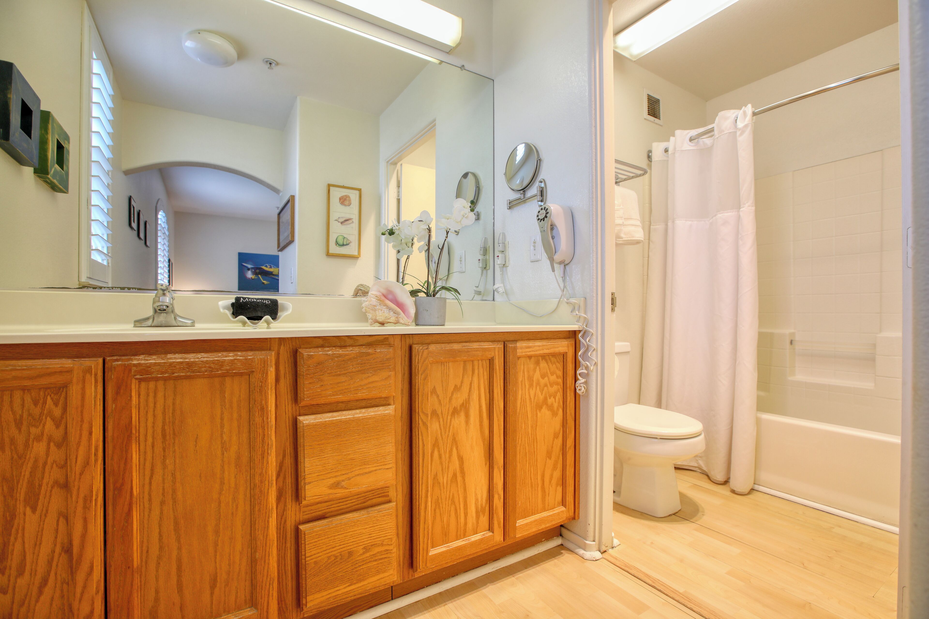 Un baño con armarios de madera, un inodoro blanco, una ducha con cortina blanca y un espejo sobre el lavabo.
