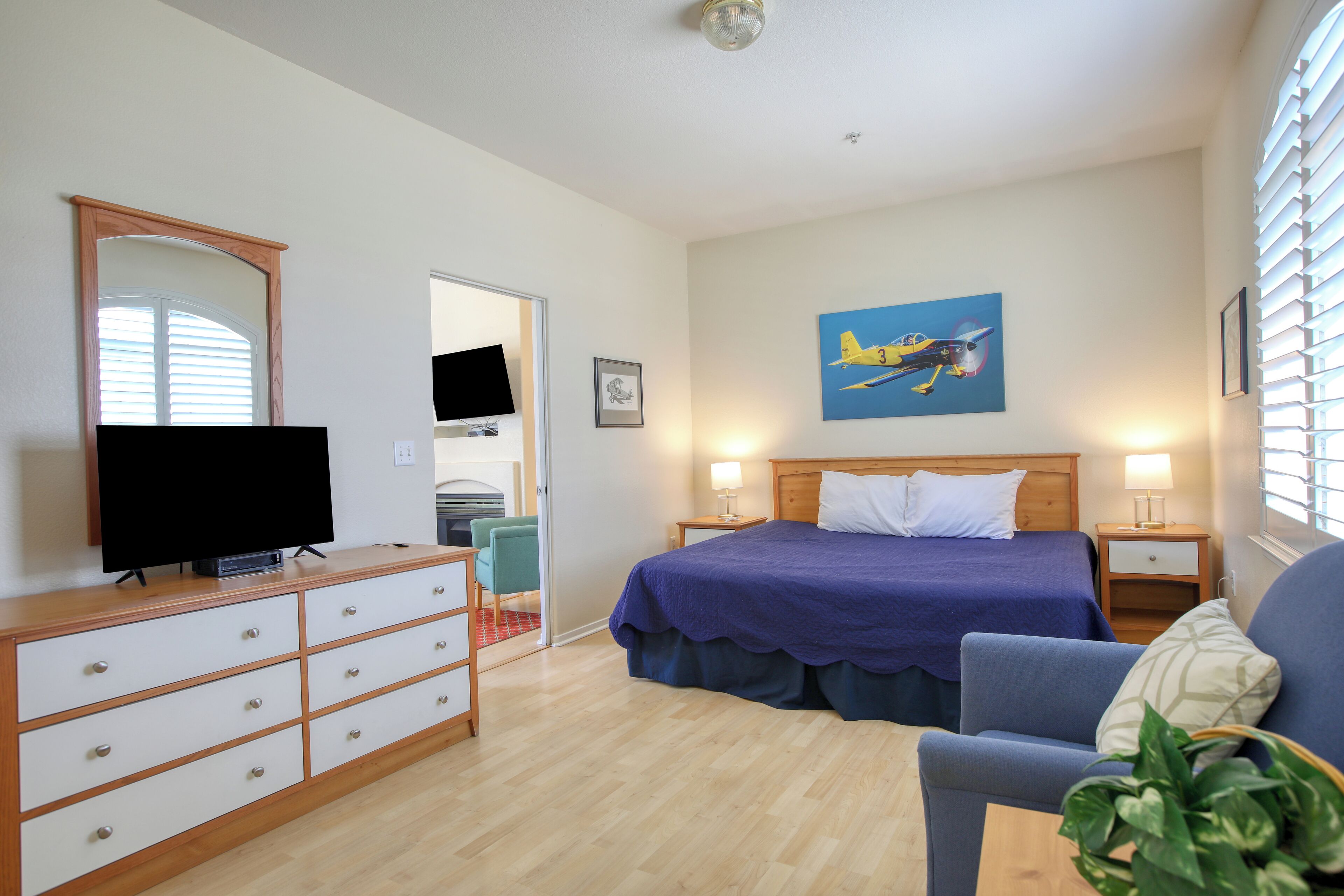 A bedroom with a bed, a TV, a dresser, a chair, and a painting on the wall.