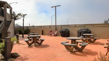 An outdoor patio area with stone tables and chairs, a barbecue grill, and a covered seating area.