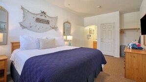 A bedroom with a large bed, a decorative wall piece, a mirror, and a door leading to another room.