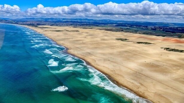 An aerial view of a coastal landscape with a sandy beach and clear blue waters.