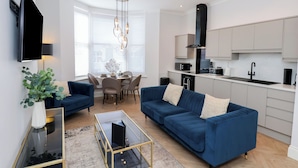 Ein modernes Wohnzimmer mit einem blauen Sofa, einem Glastisch und einem Flachbildfernseher.